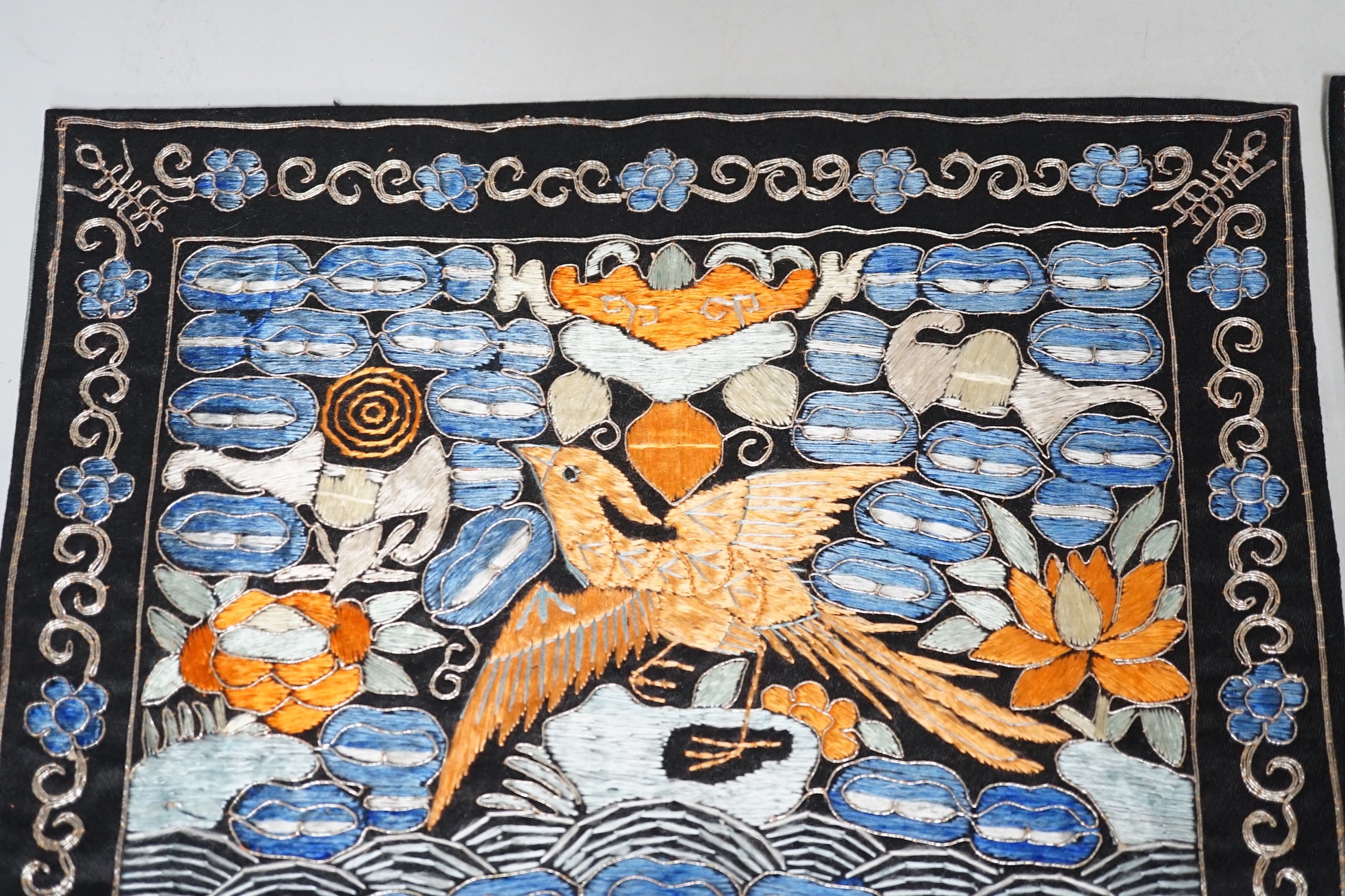 Two Chinese 20th century Chinese rank badges, embroidered I’m metal and coloured silk threads on a black ground, with a central Phoenix surrounded by auspicious symbols, 27cms x 25cms